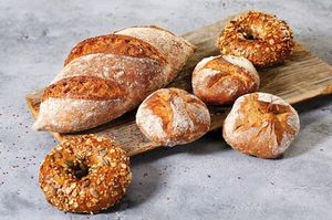 Ein Brot, drei Brötchen und zwei Bagels aus IREKS PROTEIN BREAD liegen angerichtet auf einem Brett