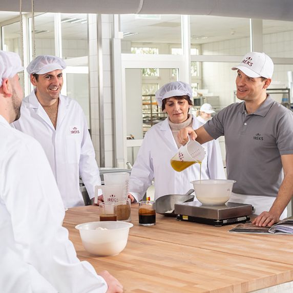 Baker showing a dough composition to a group of people in the bakery